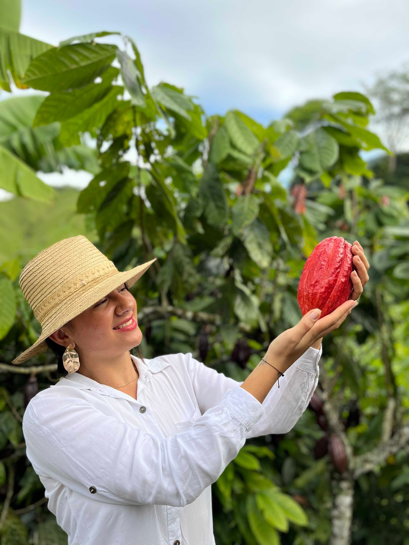 Una mujer sostiene un fruto de cacao entre los cultivos