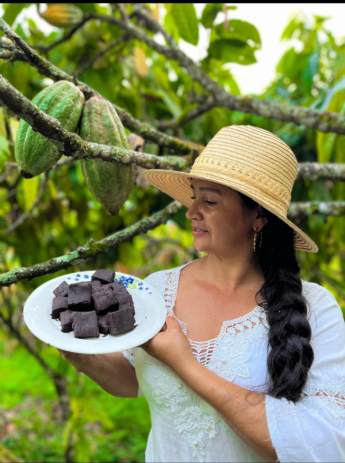 Una mujer sostiene un plato de chocolate entre árboles de cacao