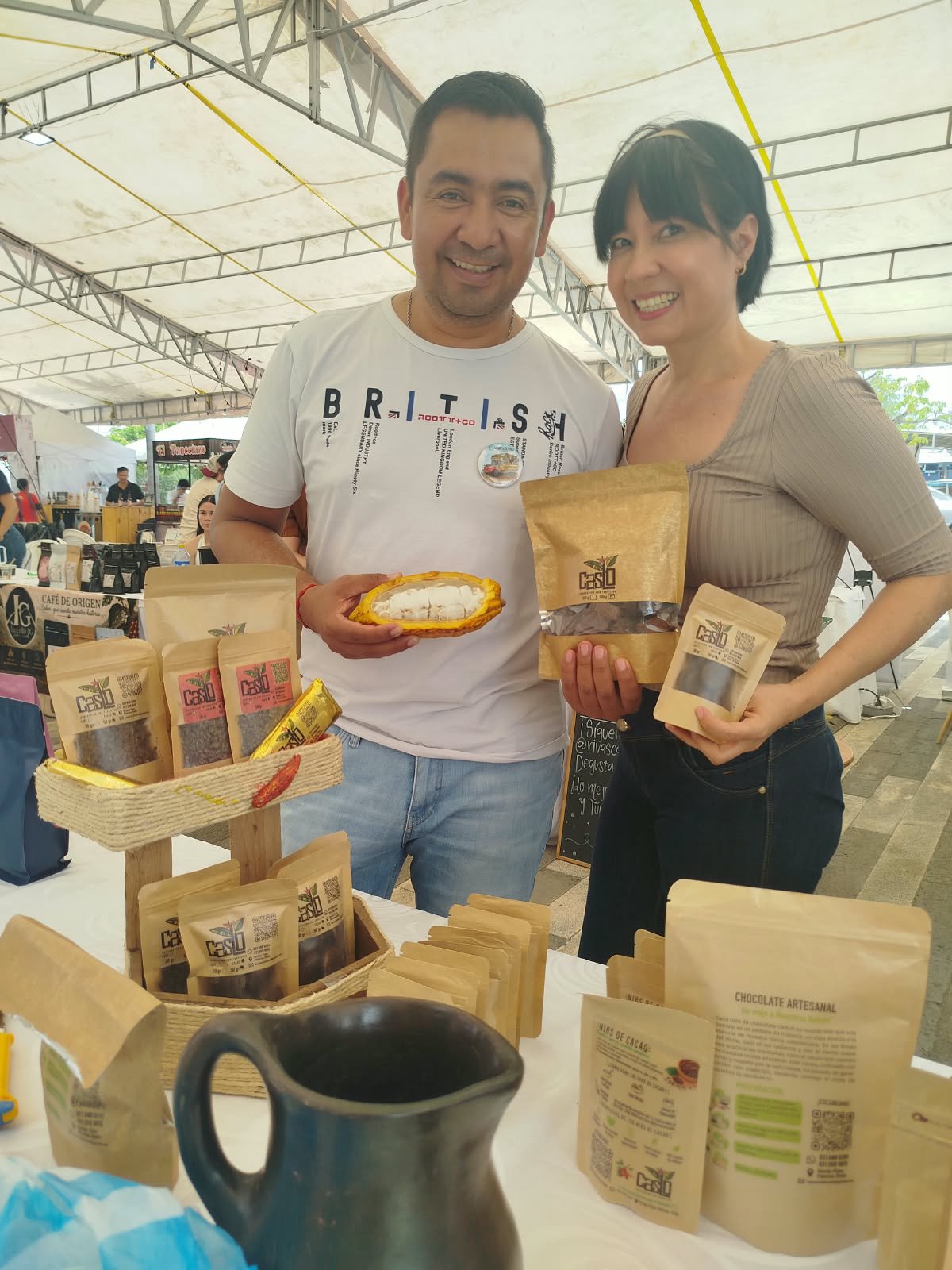 Dos personas presentan productos CASLO y un fruto de cacao en un puesto de feria
